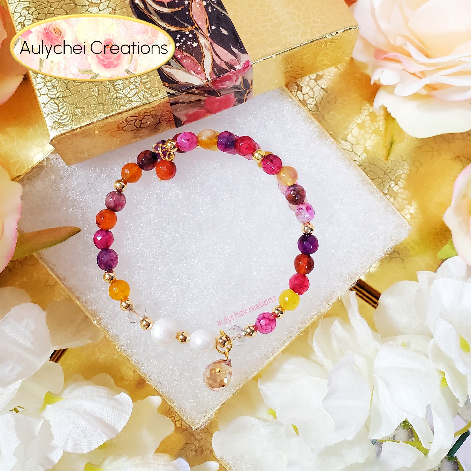 Colorful multi-color pink gemstone beaded bracelet on white cushion stand with floral decorations and 'Aulychei Creations' branding.