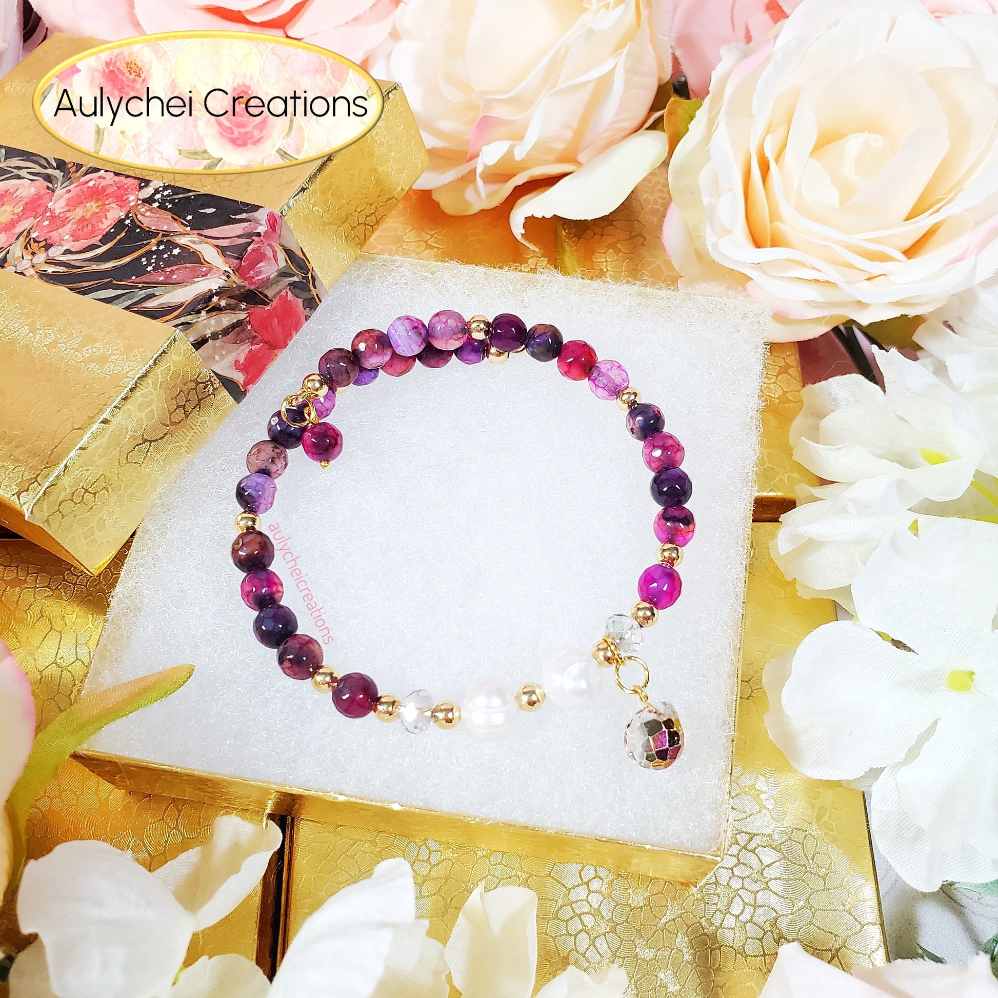 Multicolored dark magenta gemstone beaded bracelet on a white card with flowers and decorative elements in the background, featuring 'Aulychel Creations'.