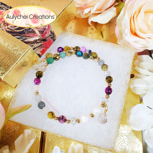 Multicolored beaded bracelet on a white stand with flowers and gold accents in the background, featuring 'Aulychei Creations' branding.