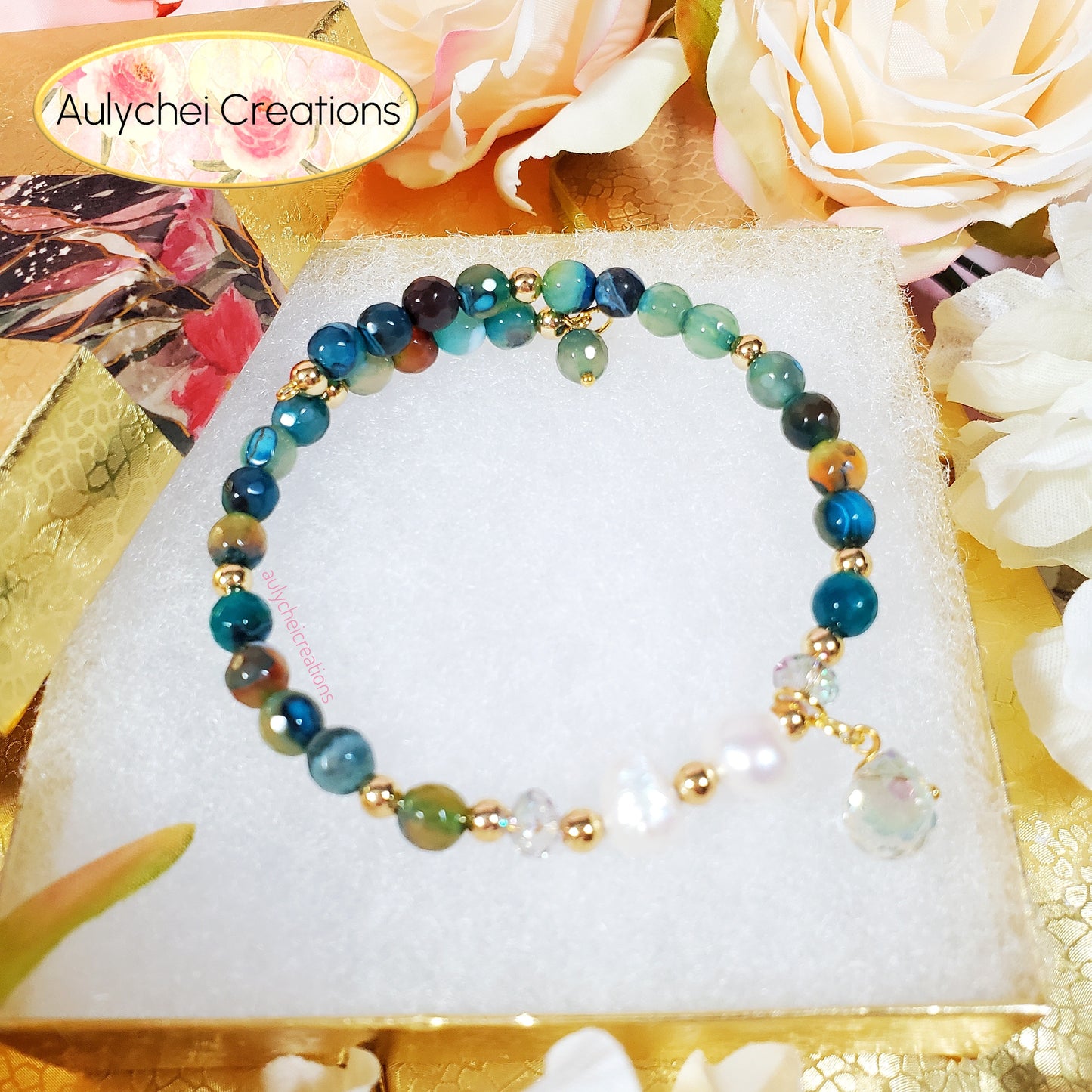 Multicolored turquoise gemstone beaded bracelet on a white stand with flowers in the background, featuring 'Aulychei Creations' branding.
