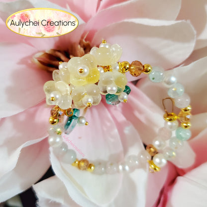 Beaded bracelet with flowers on a pink flower background, featuring 'Aulychei Creations' branding.